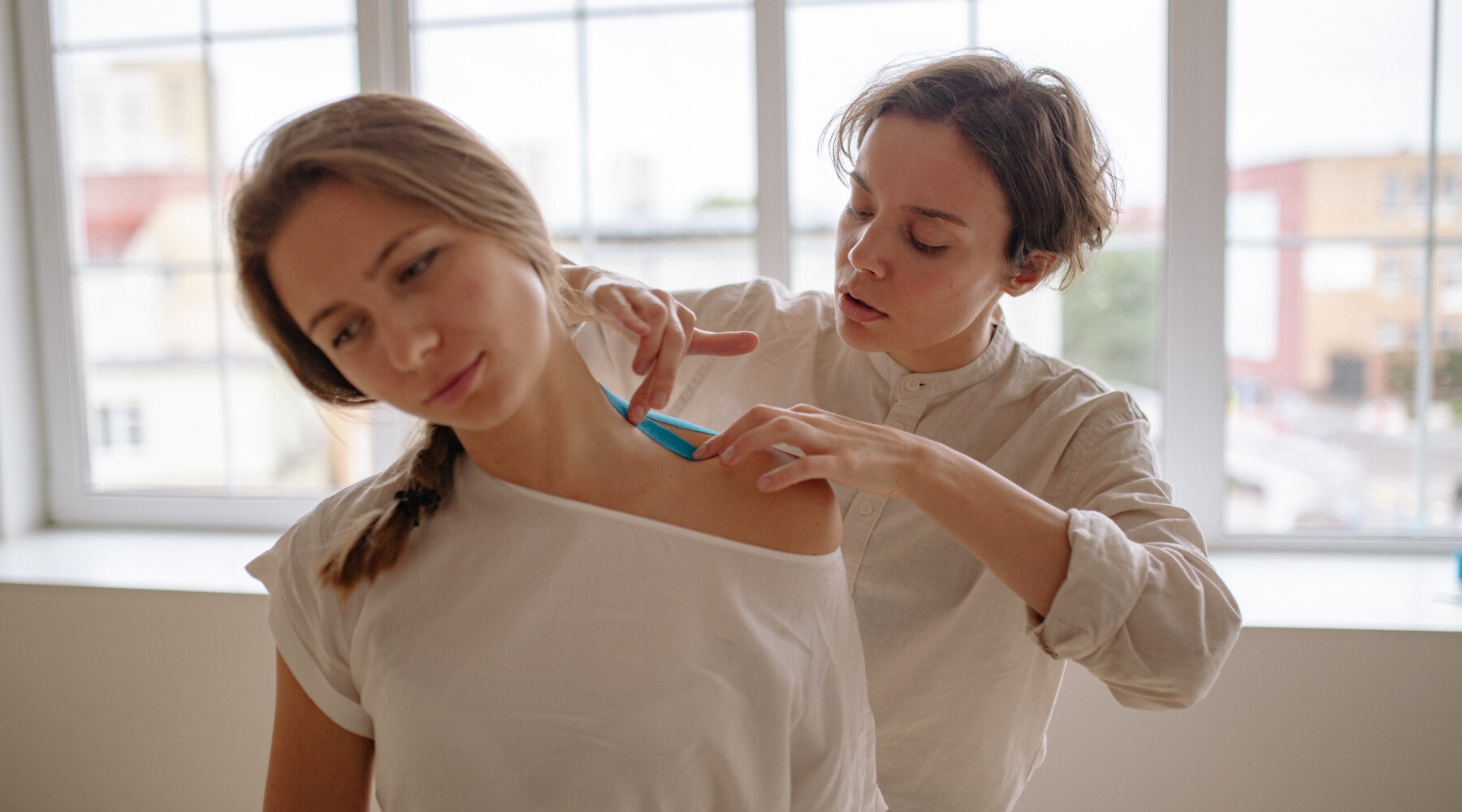 A woman applies bandage to a woman's neck.