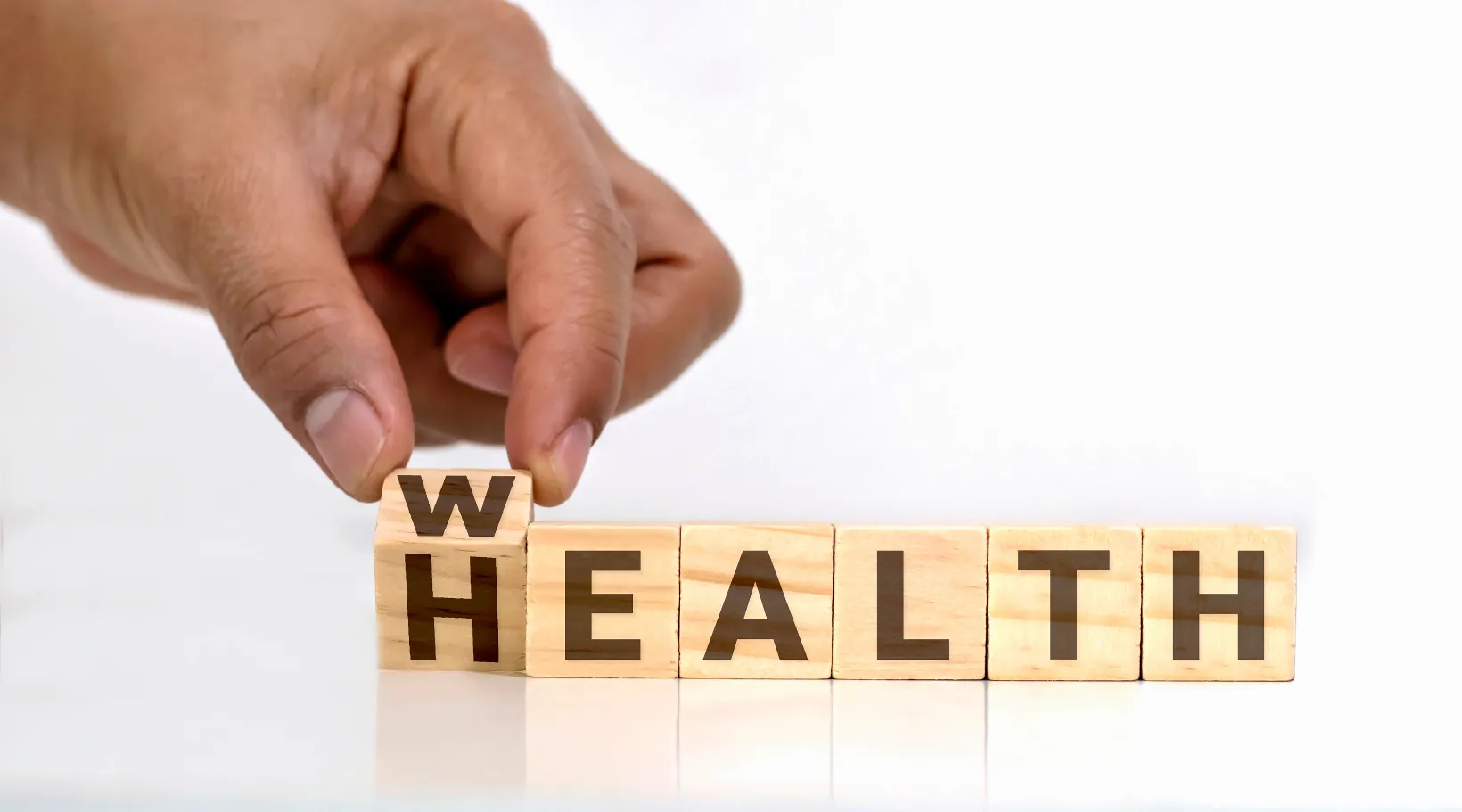Hand changing ‘HEALTH’ to ‘WEALTH’ with wooden cubes symbolizing prosperity, ShiftCare.