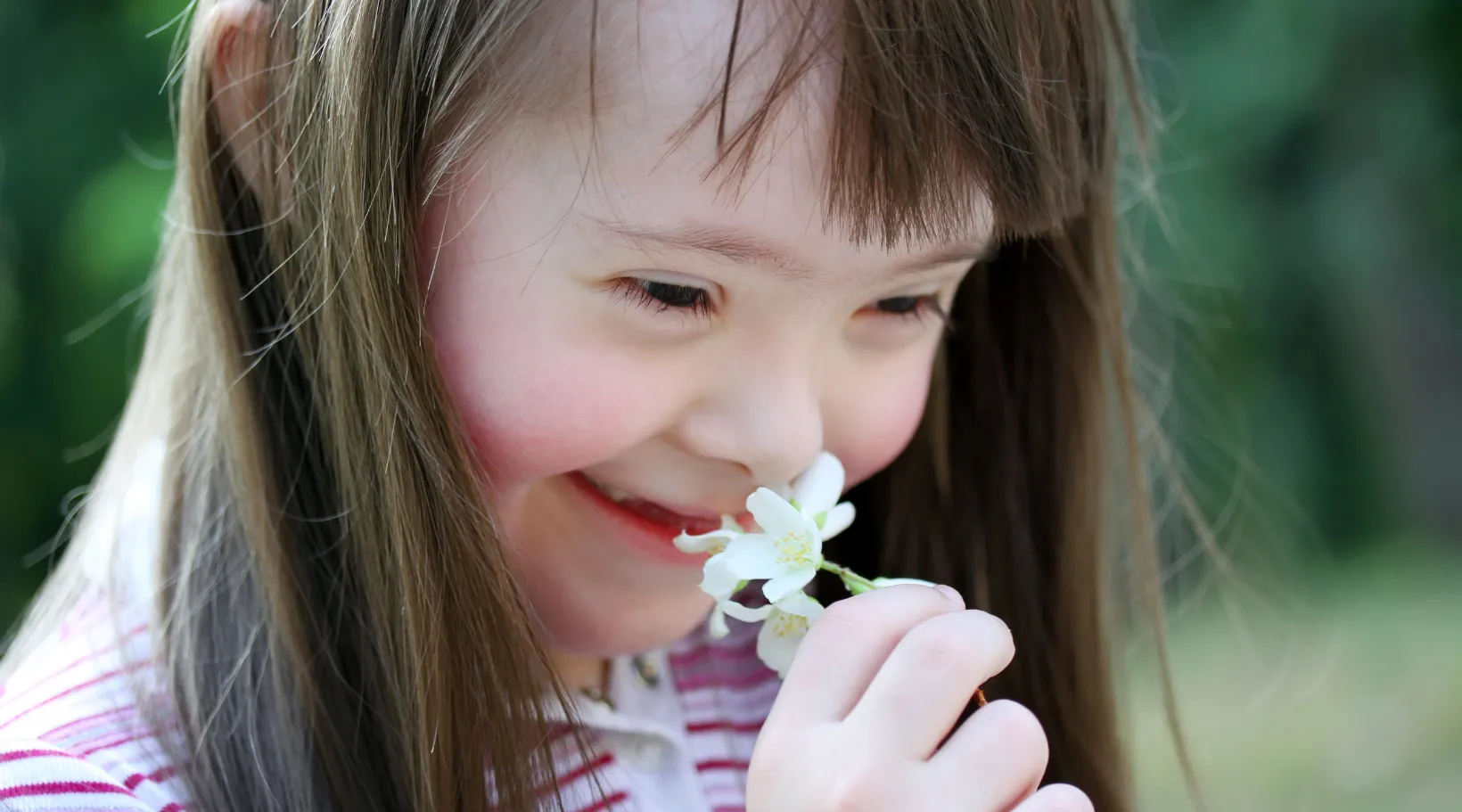 Happy girl smiling while smelling a delicate white flower, ShiftCare.