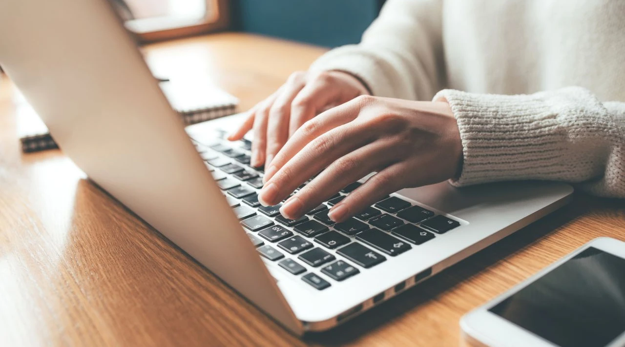 Close-up of hands typing on a laptop at a desk, representing digital care management and efficiency.