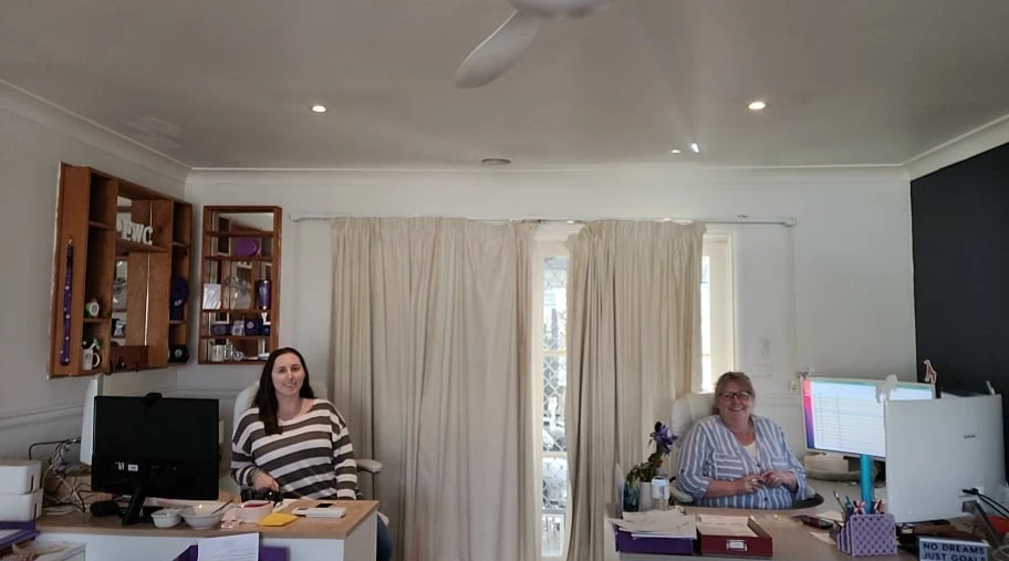Two women smiling at their desks in a community care office supporting NDIS participants.