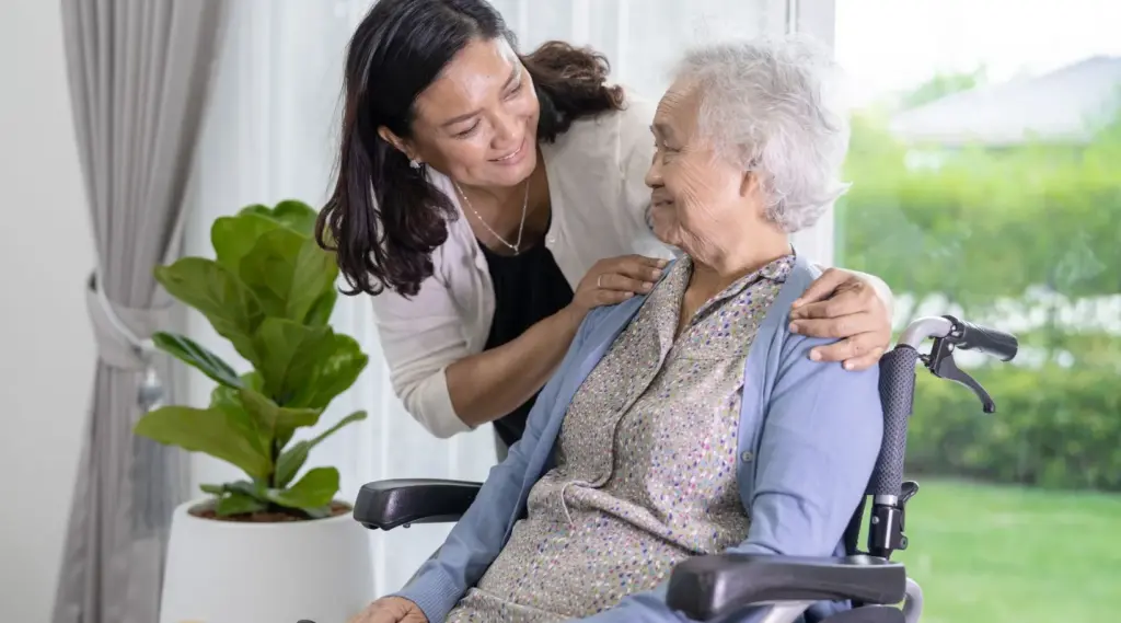 Support worker smiling while comforting elderly woman in wheelchair at home, ShiftCare.