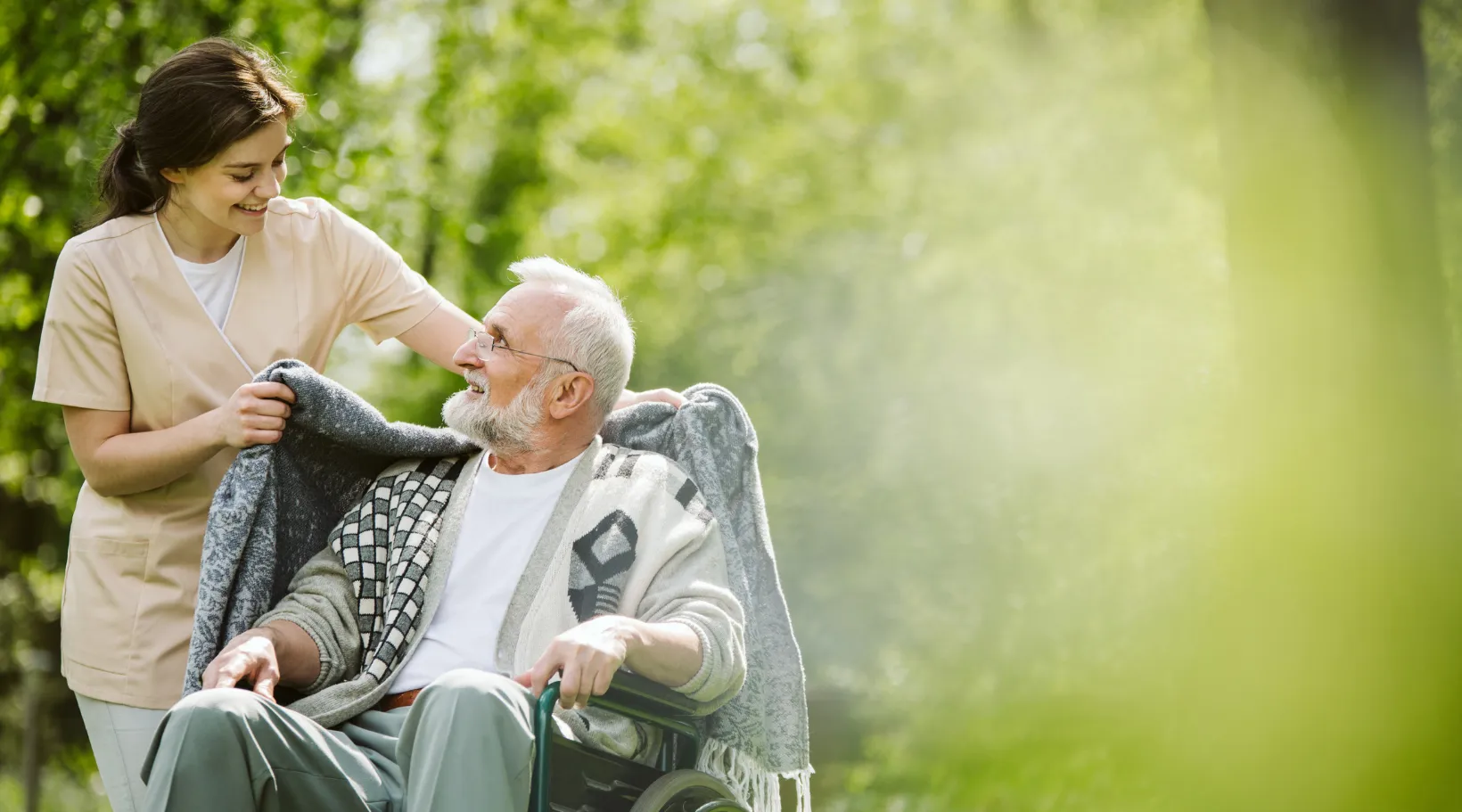 Home care worker assisting senior man in wheelchair during outdoor activity with ShiftCare.