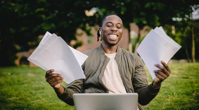Man smiling while holding papers and working on laptop during internal NDIS audit, ShiftCare.