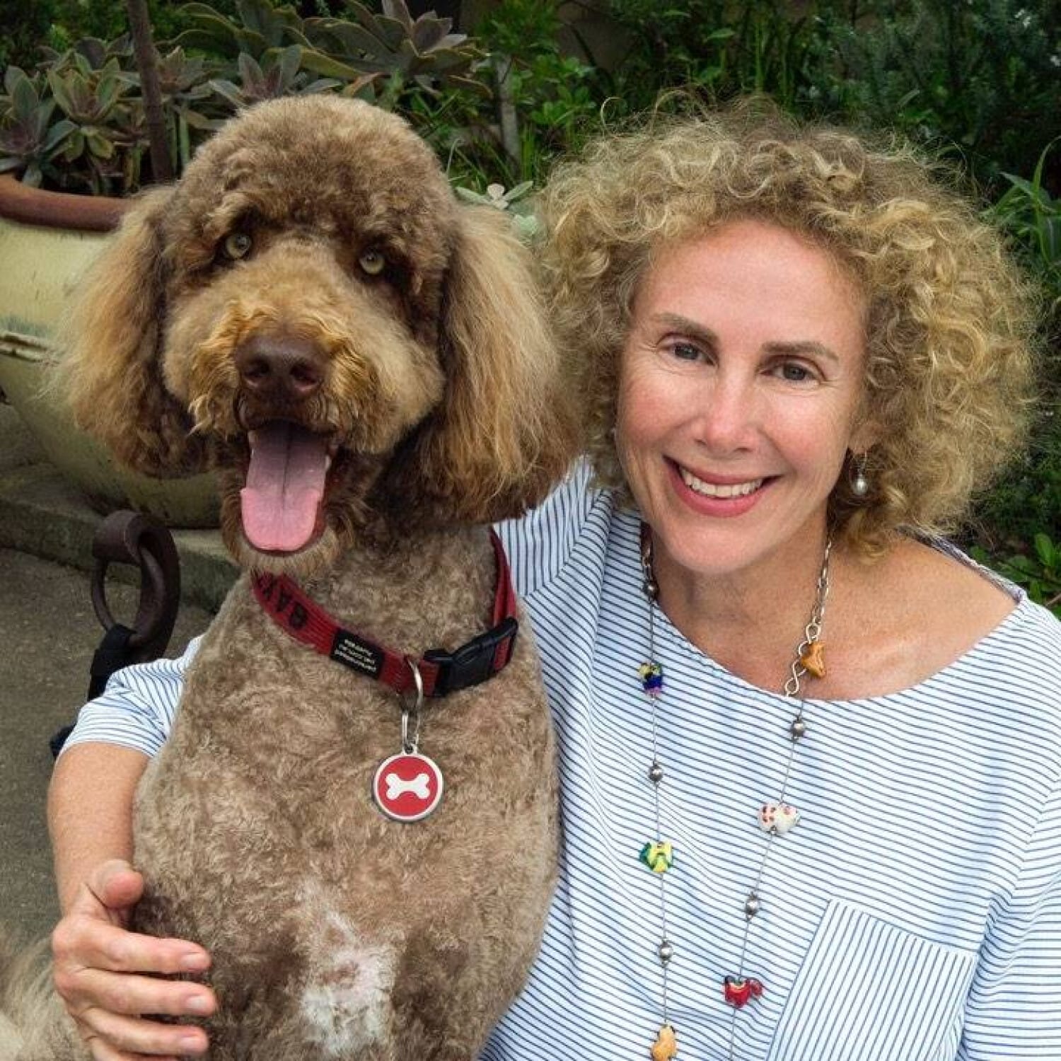 Smiling woman with curly hair and her happy brown poodle dog sitting outdoors together