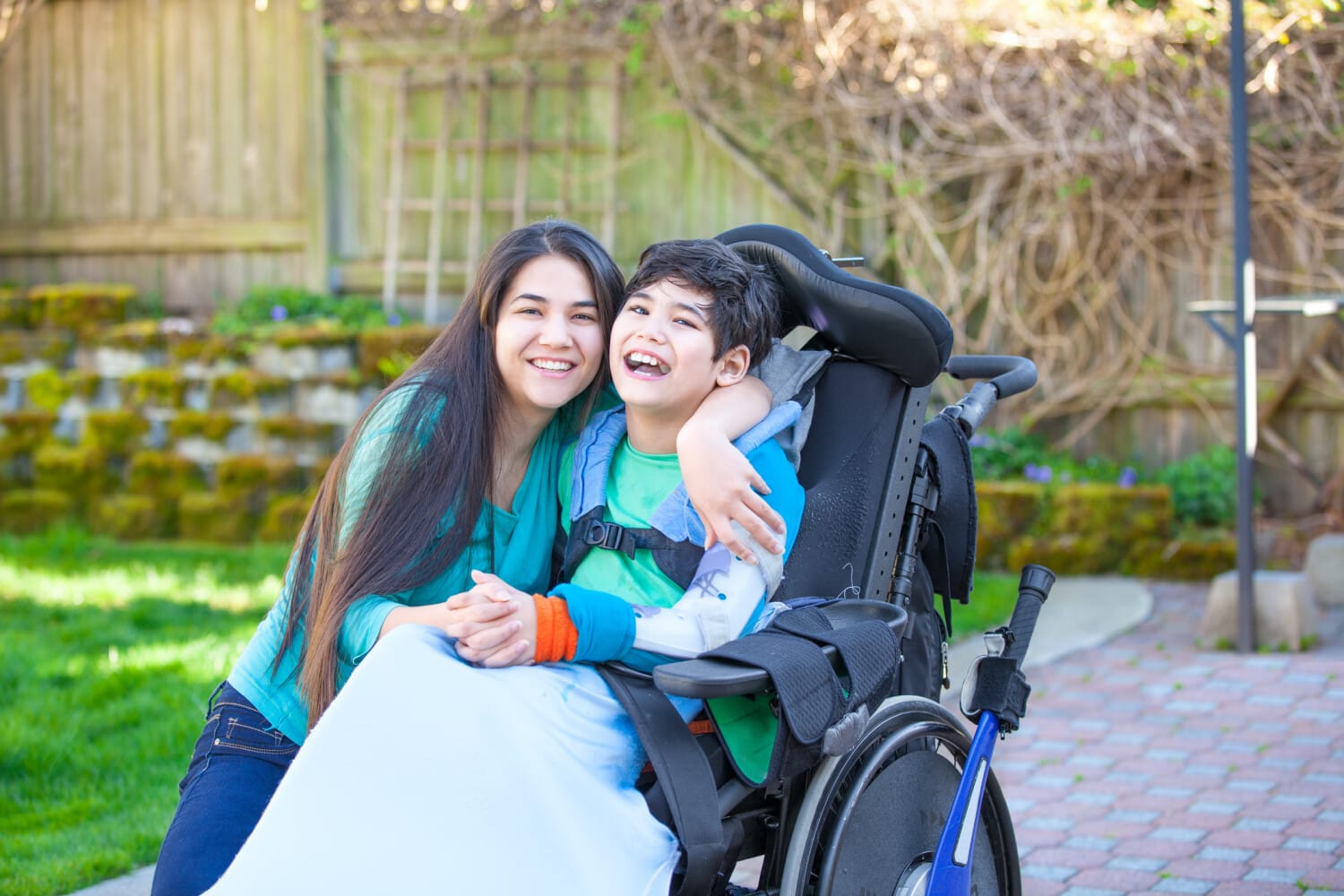 Support worker hugging a smiling boy in a wheelchair outdoors, symbolizing compassionate NDIS care with ShiftCare.