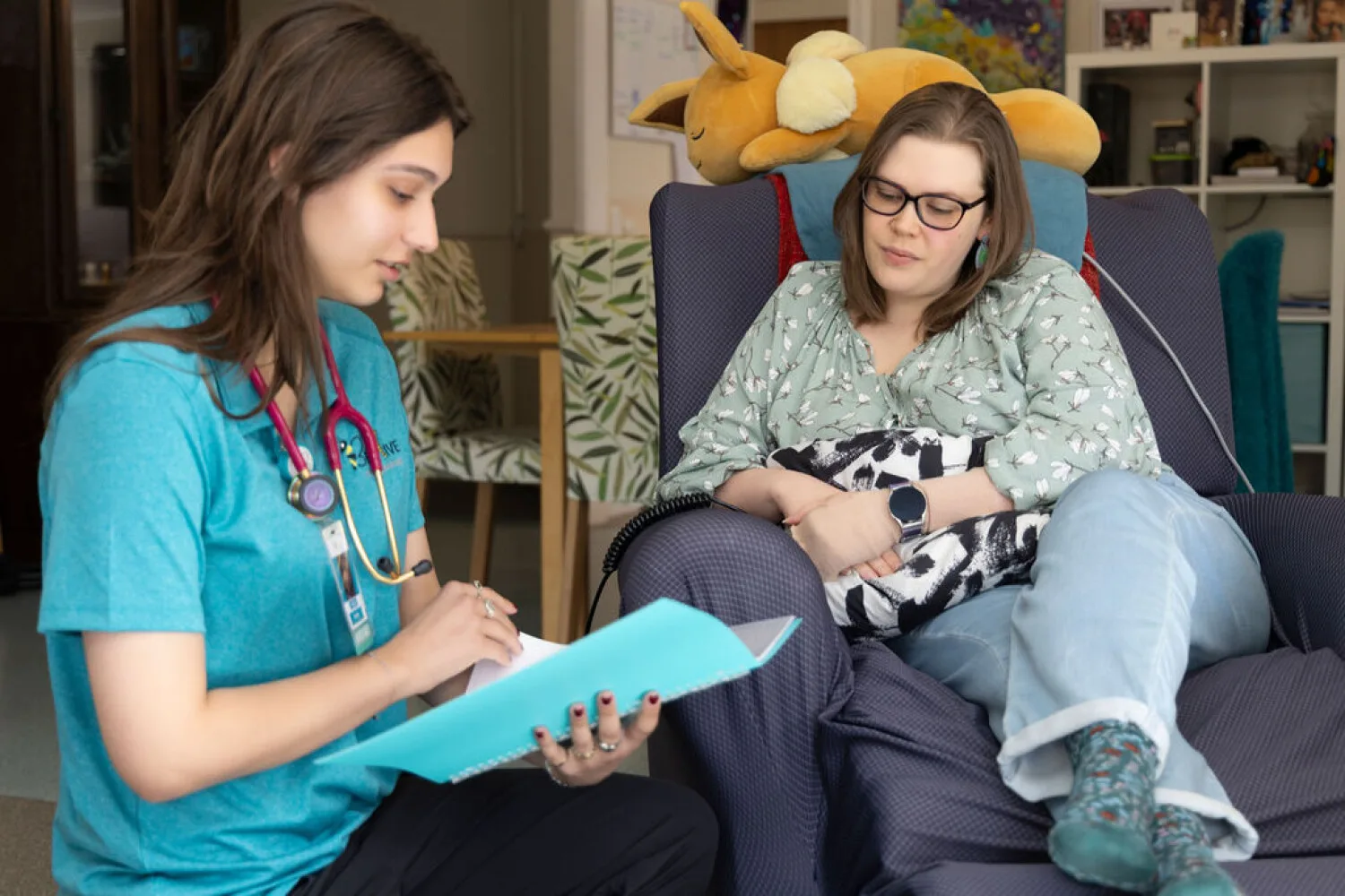 NDIS provider offering home care consultation as nurse explains support services to client in chair.