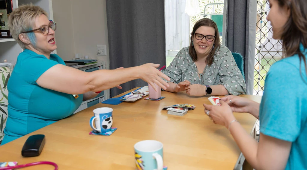 Disability care workers and client enjoying card game as part of in-home community engagement service.