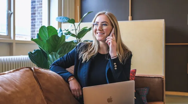 Smiling businesswoman on phone with laptop in modern office, representing ShiftCare.