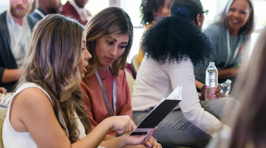 Two women reviewing notes together during a seminar, representing collaboration and learning.
