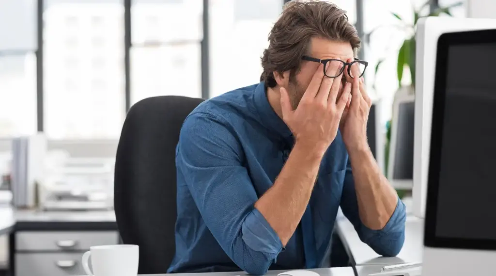 Employee feeling stressed at desk, representing workplace fatigue and support by ShiftCare.