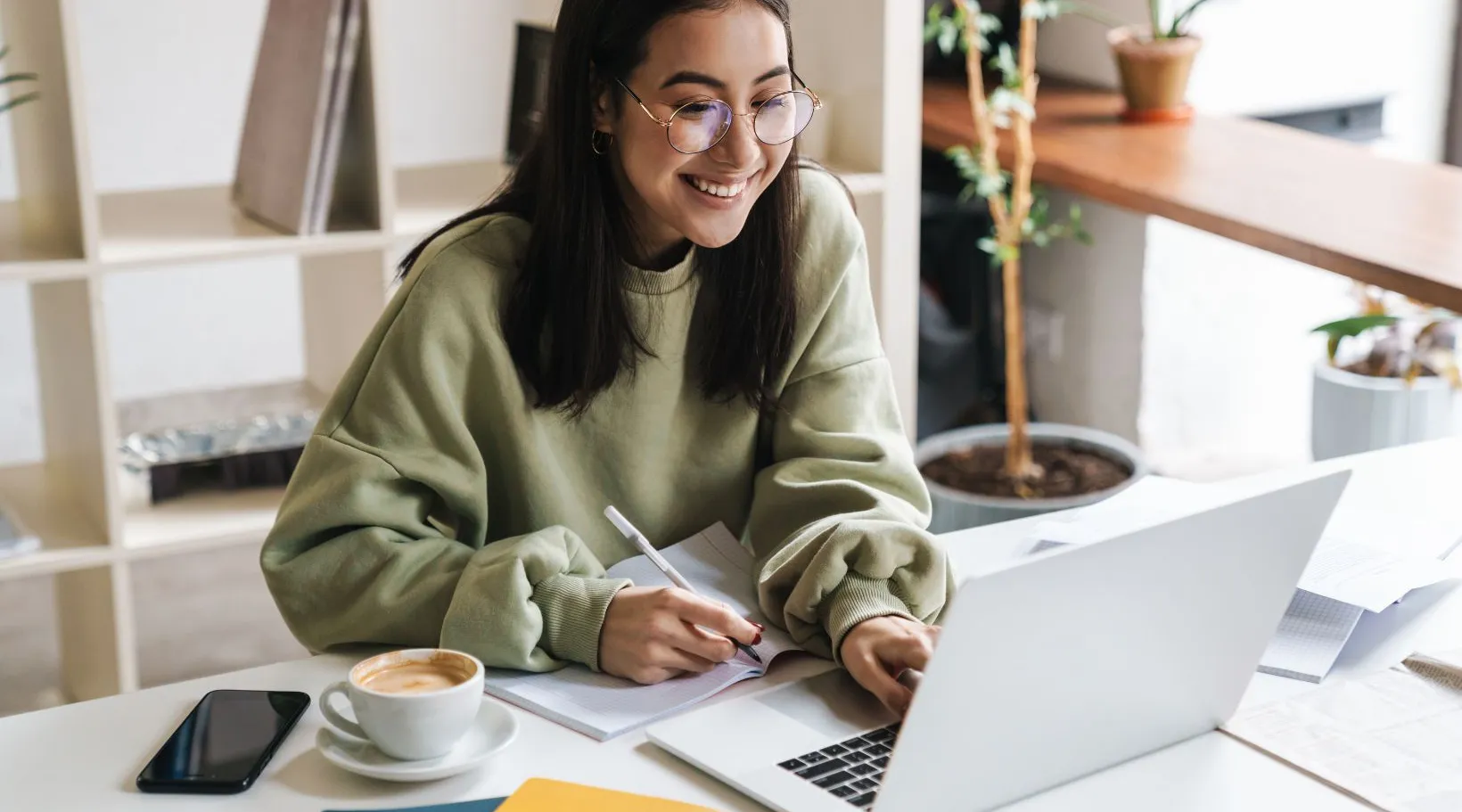 Professional woman working on laptop and taking notes in home office, ShiftCare.