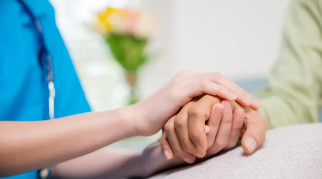 Close-up of caregiver providing reassurance by holding client’s hand during care