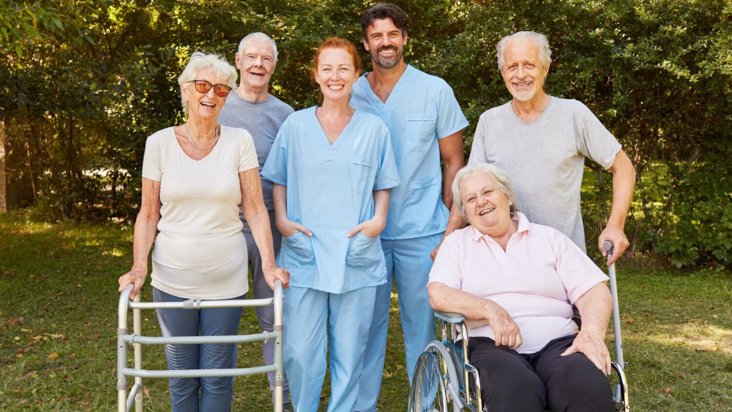 Senior care group with support staff providing assistance to elderly people in a garden setting