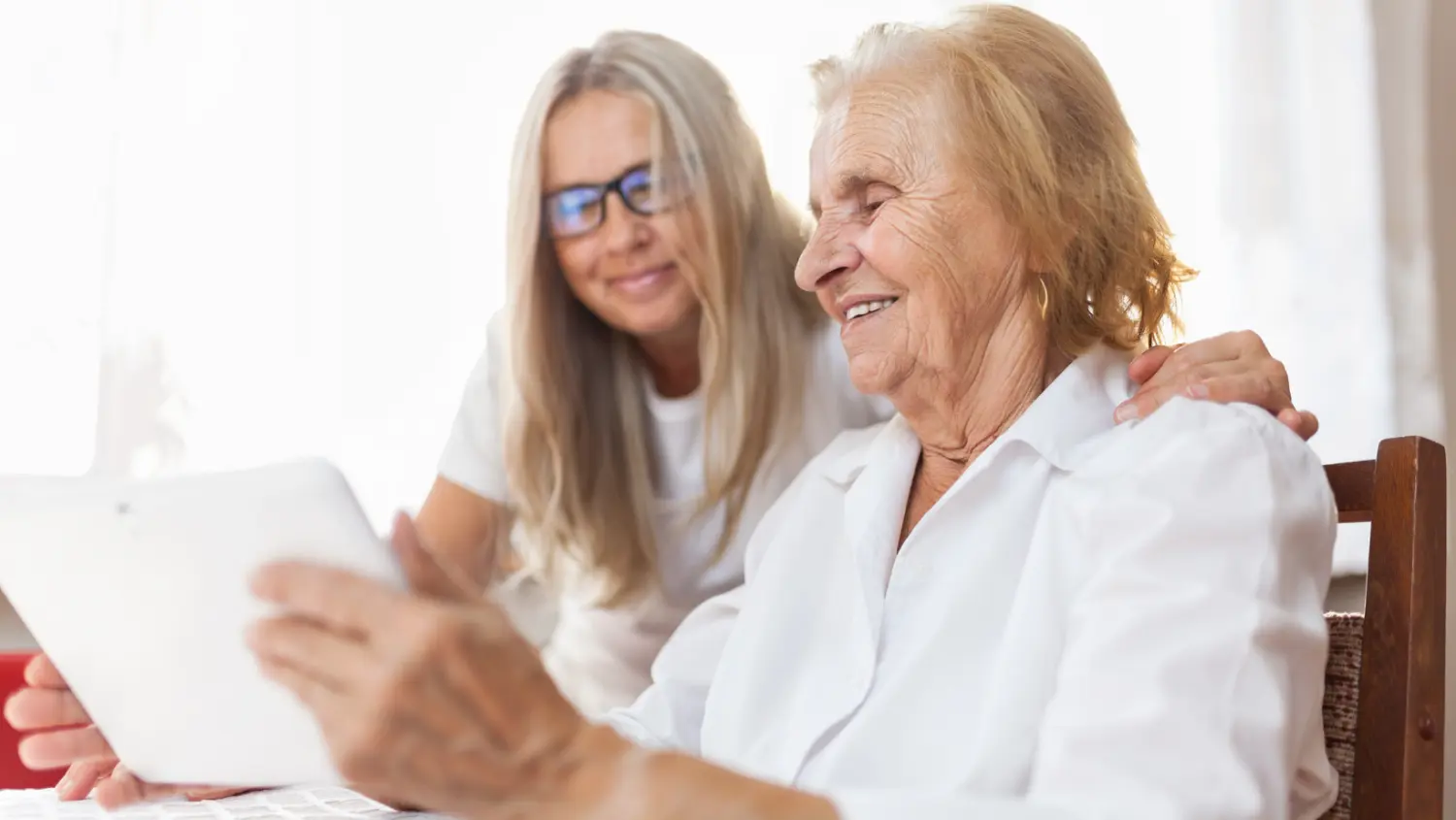 Caregiver assisting senior client using tablet during home care visit for communication and support.