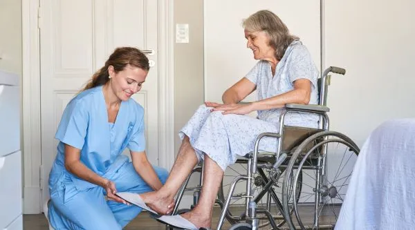 Nurse helping senior woman in wheelchair during daily home care routine, ShiftCare.
