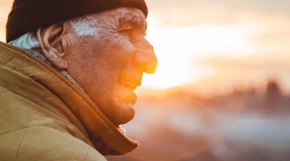 Elderly man smiling warmly in the sunlight, symbolizing wellbeing and positive aging.