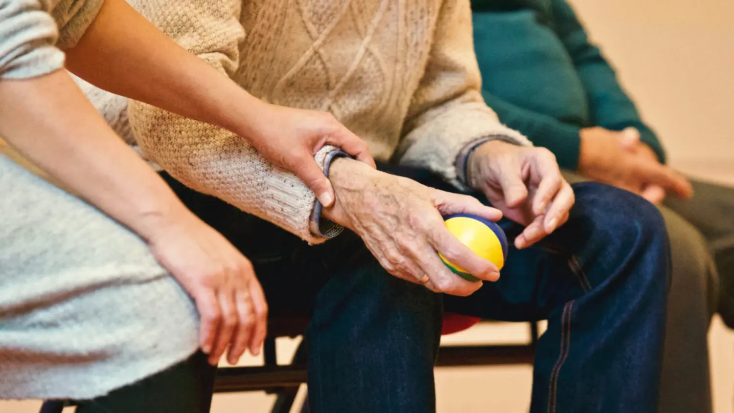 Elderly person holding a therapy ball with caregiver assistance, ShiftCare.