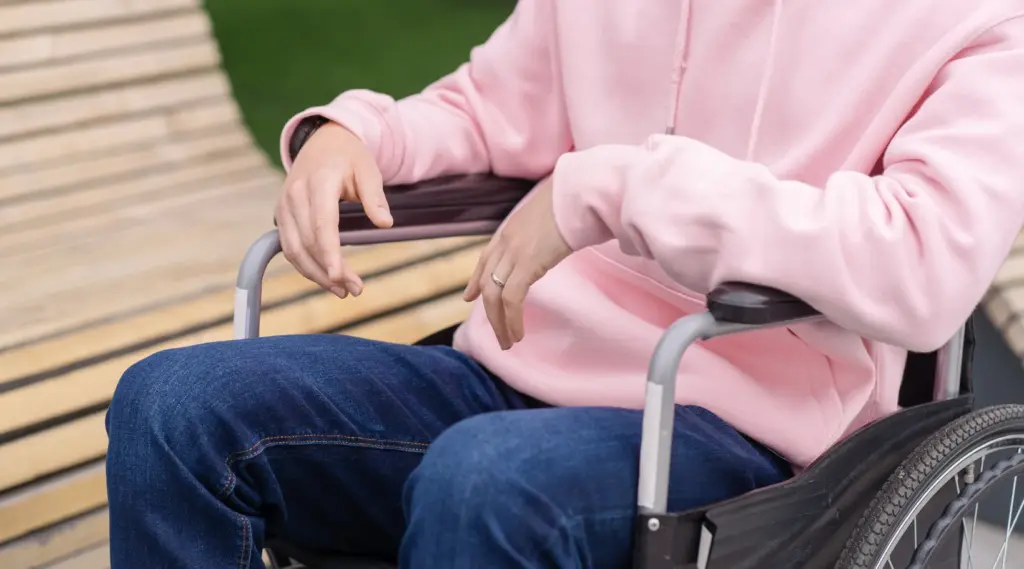 Person in wheelchair wearing pink hoodie outdoors, ShiftCare.