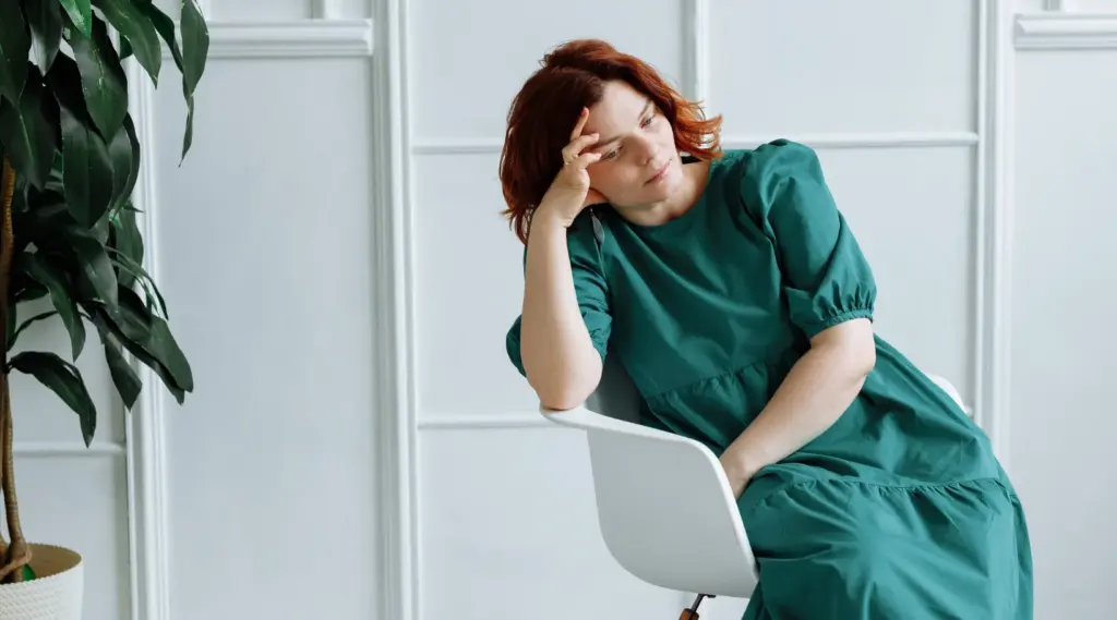Exhausted caregiver in green dress sitting pensively, highlighting the need for ShiftCare support.