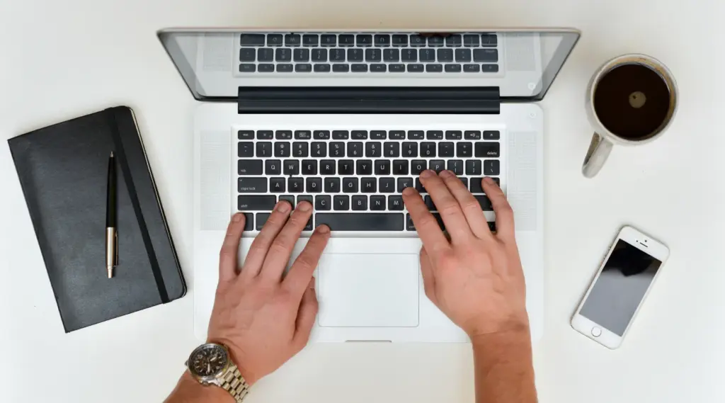 ShiftCare user managing care operations on a laptop with notes, coffee, and phone nearby.