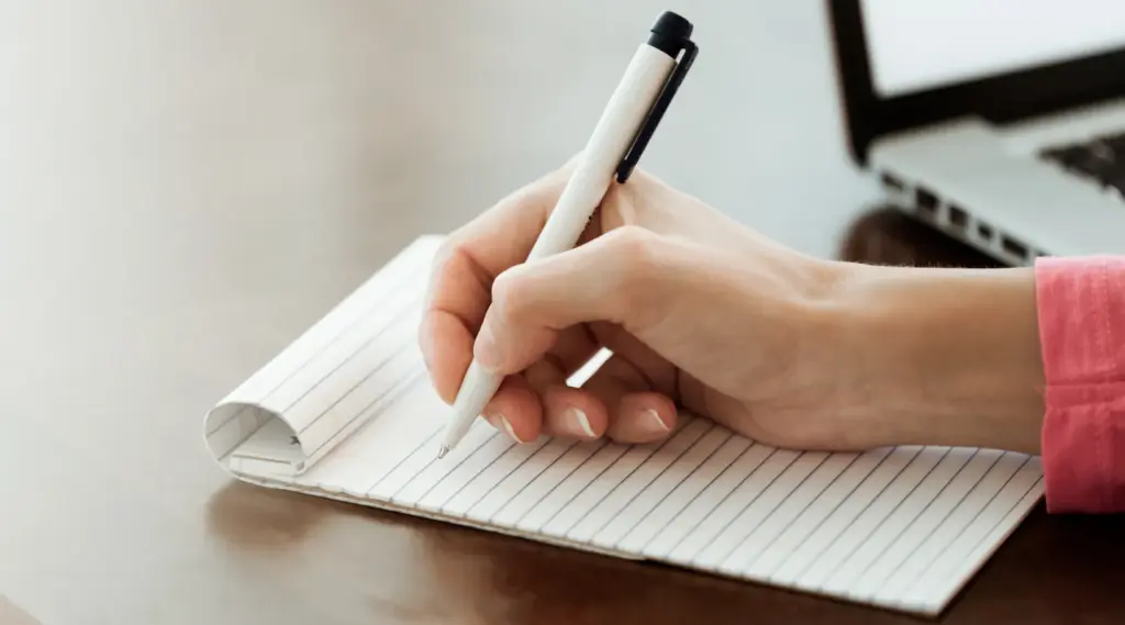 Writing notes beside laptop representing focus and efficiency with ShiftCare.