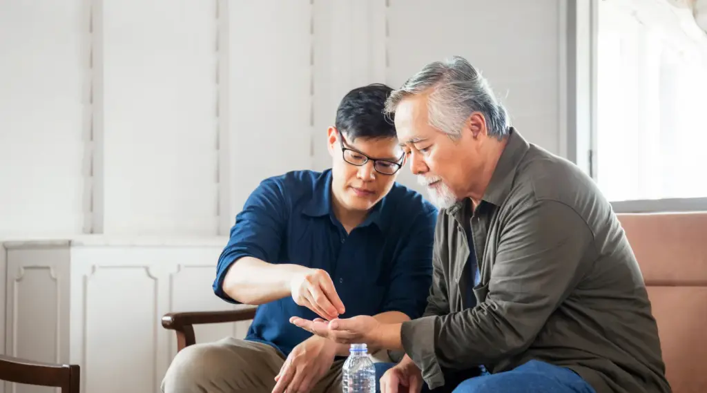 Caregiver assisting elderly man with medication at home using ShiftCare software.