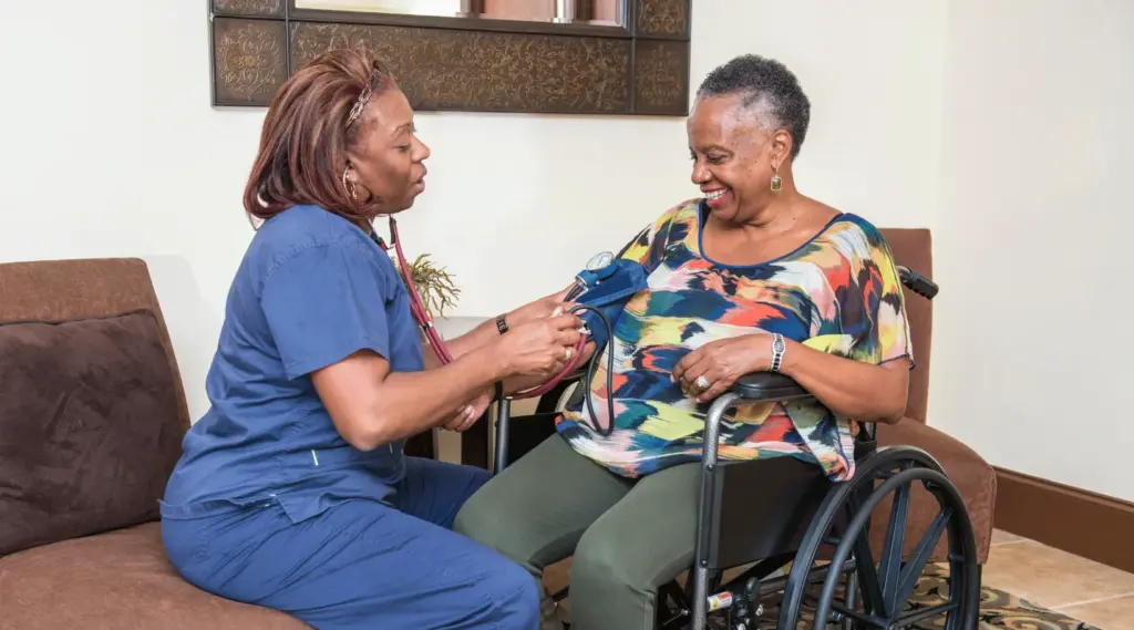 Home care nurse using ShiftCare app to check blood pressure of a smiling senior client.