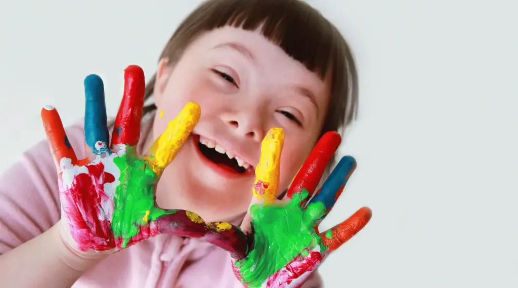 Child enjoying creative art-therapy activity with colourful paint on hands, ShiftCare.
