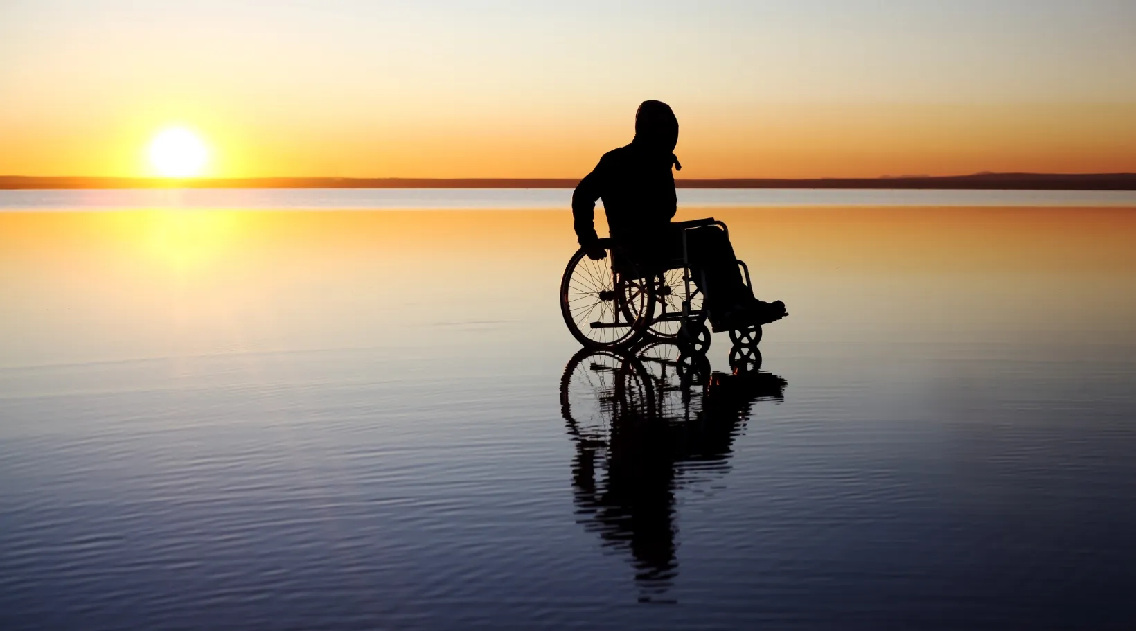 Person using wheelchair by the water at sunset representing independence supported by home care services.