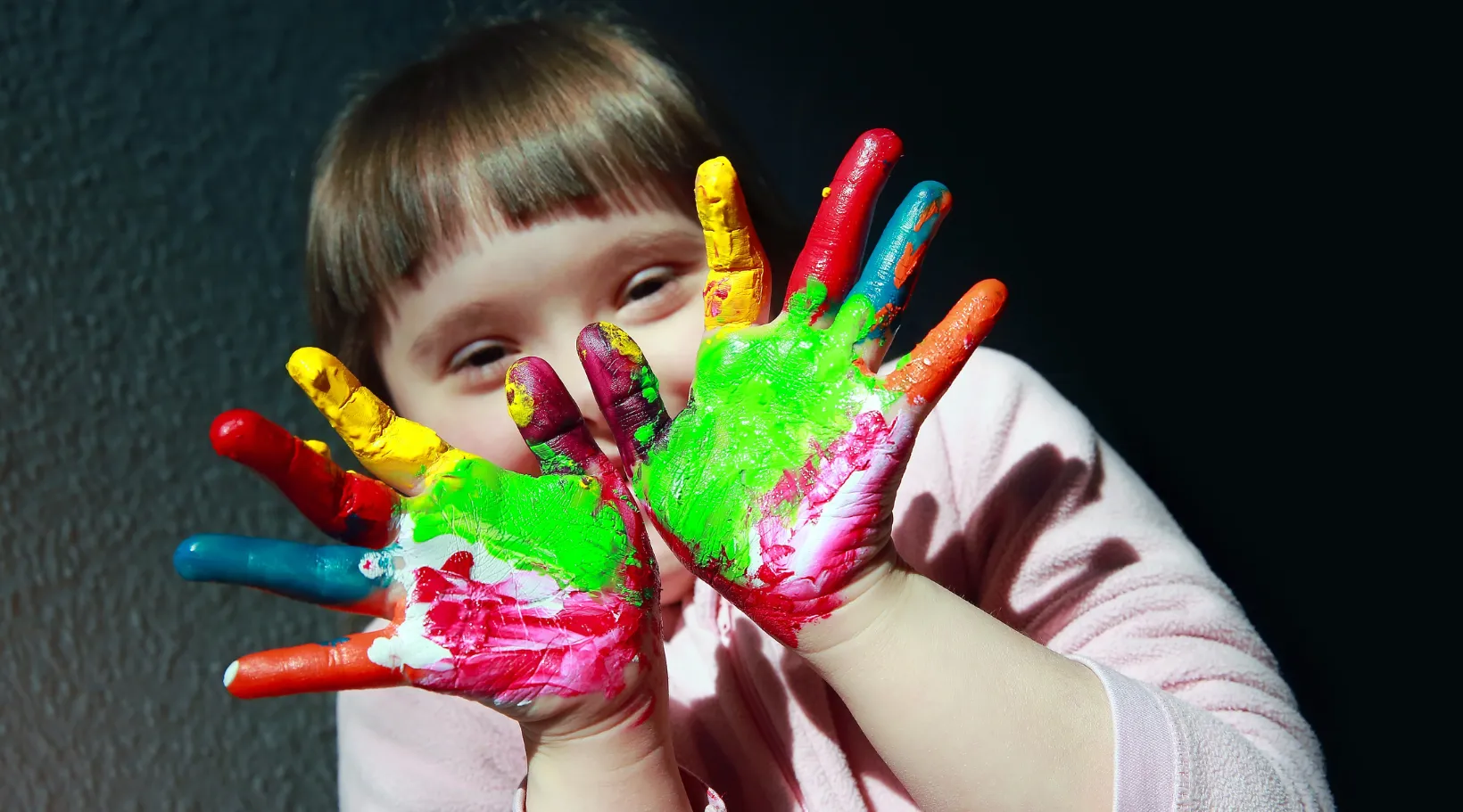 Child enjoying creative art therapy activity with colorful paint on hands, ShiftCare.