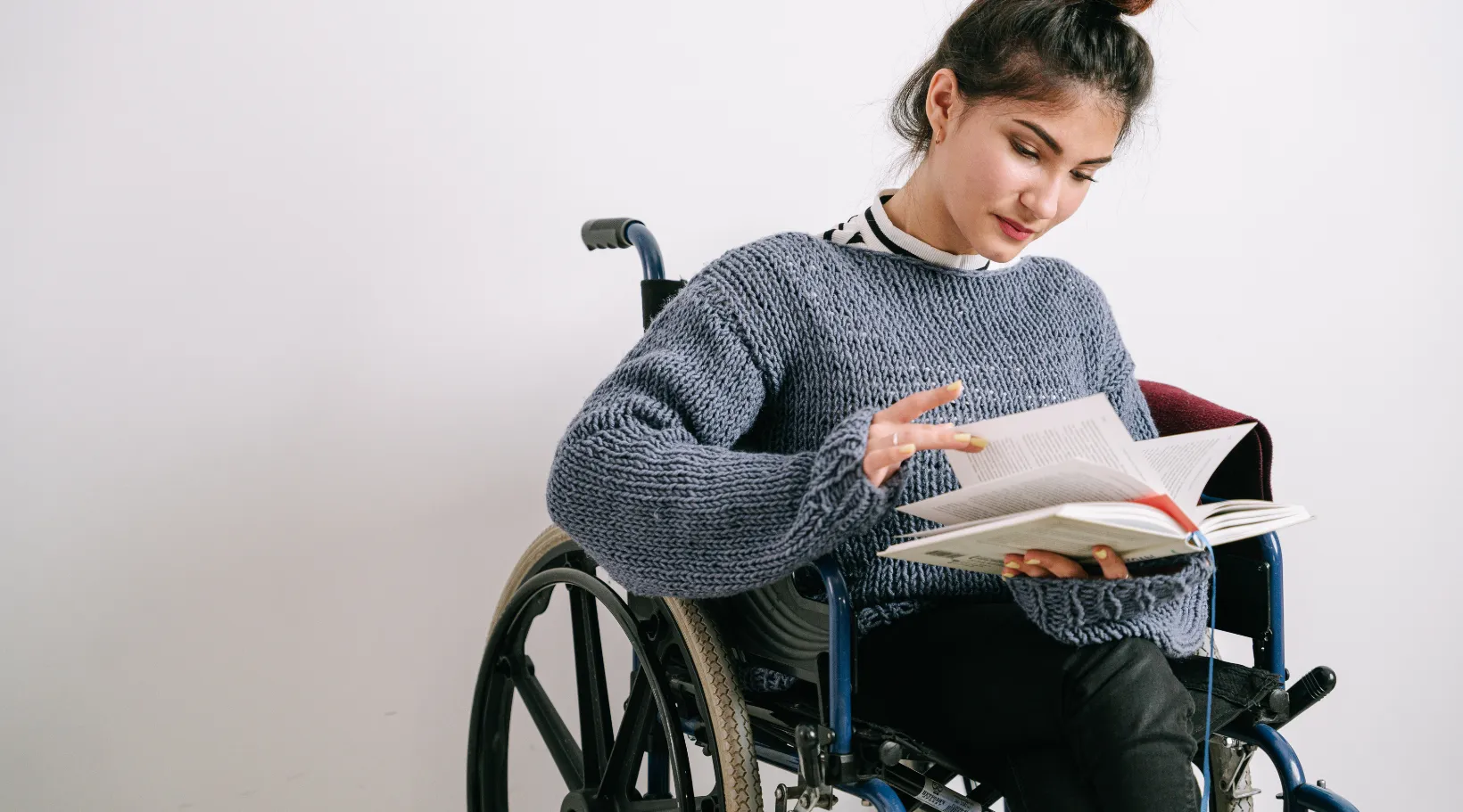 Young woman in a wheelchair reading a book, symbolizing independence and empowerment in care.