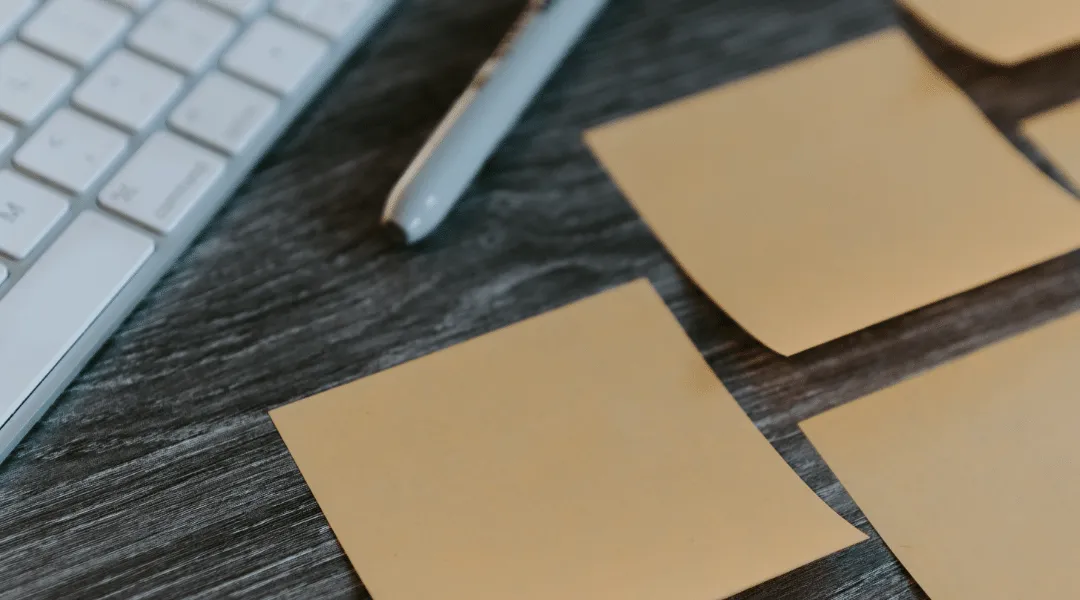 Sticky notes and pen beside keyboard on desk for task planning, ShiftCare.