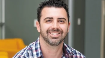 Man in casual office setting smiling confidently, possibly team member or leader in NDIS services.