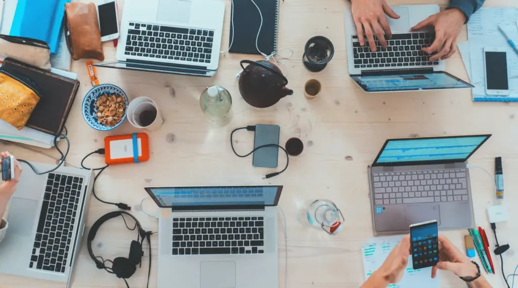 Team using laptops and phones in creative workspace with ShiftCare.