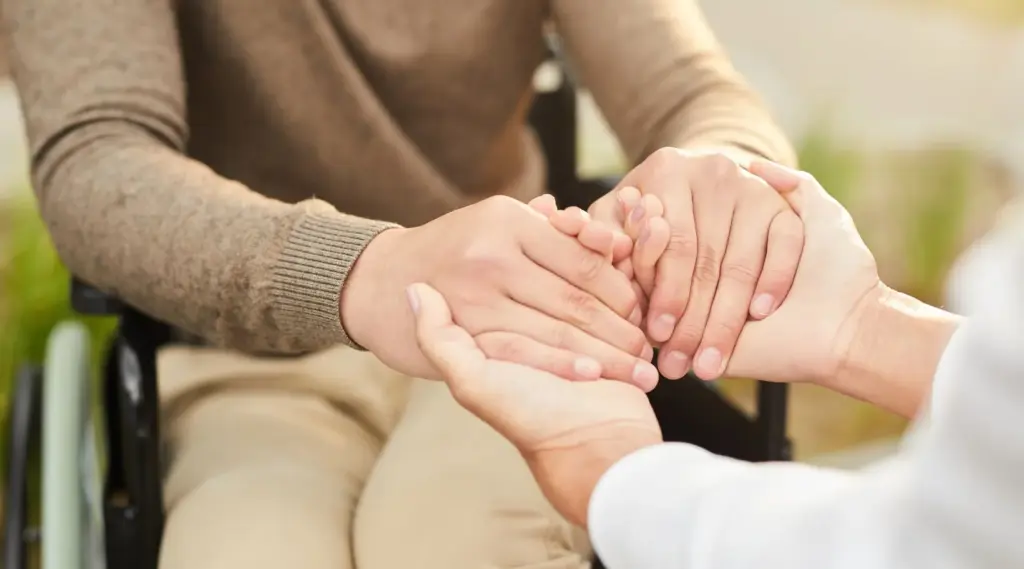Caregiver holding hands of wheelchair user during supportive home care visit.