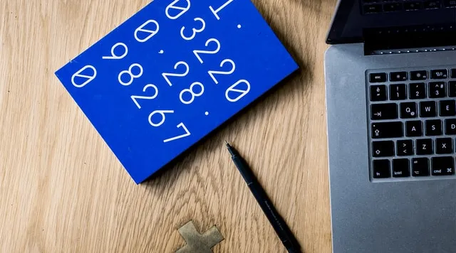 NDIS price guide 2020 update with blue notebook, pen, and laptop on desk by ShiftCare.