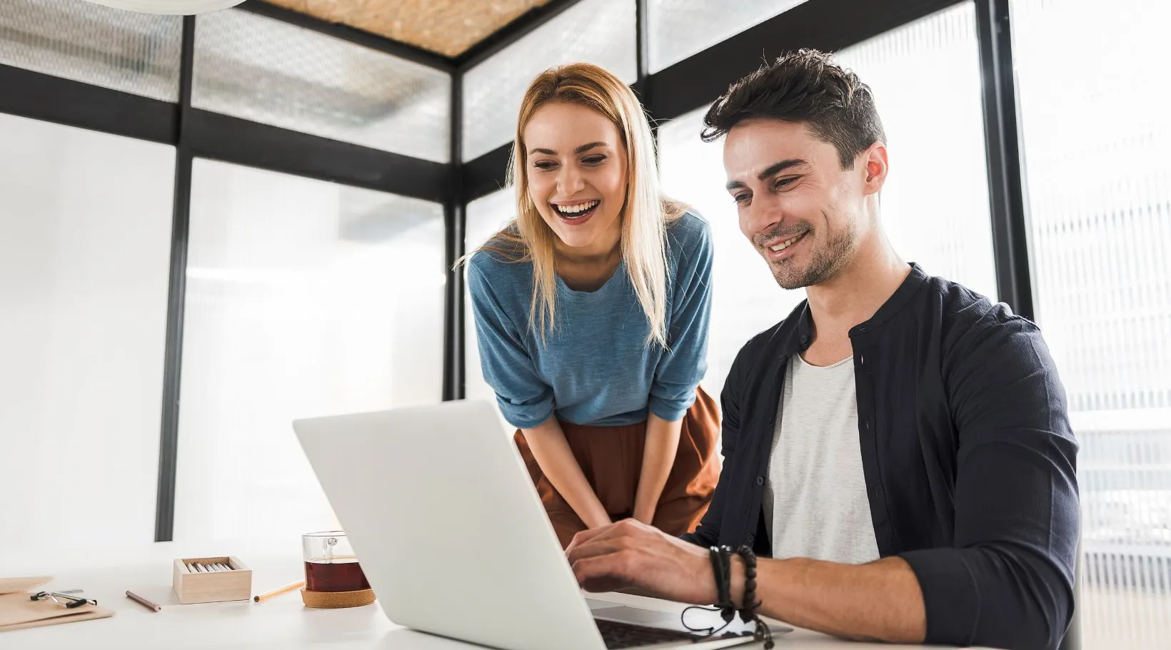 Two colleagues smiling while working on laptop in bright office, ShiftCare.