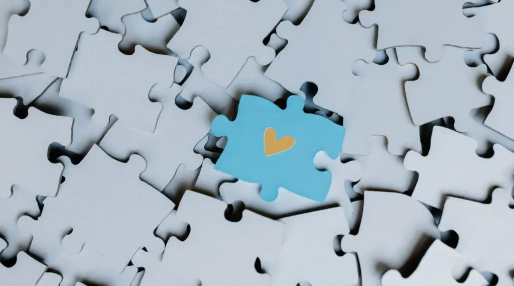 Blue puzzle piece with a heart among white pieces, symbolizing care, unity, and compassion.