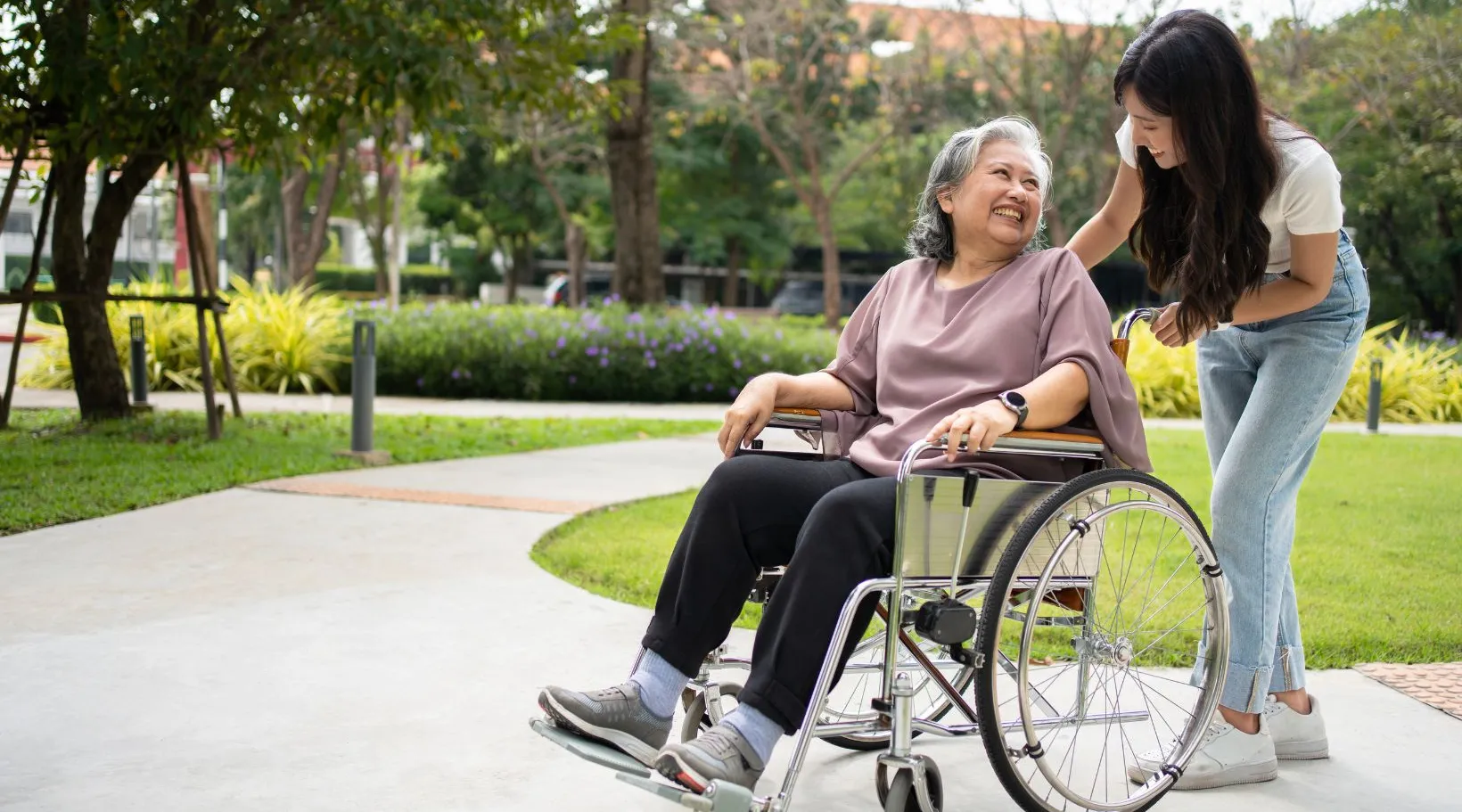 Caregiver assisting an elderly woman in a wheelchair enjoying a walk outdoors, by ShiftCare.