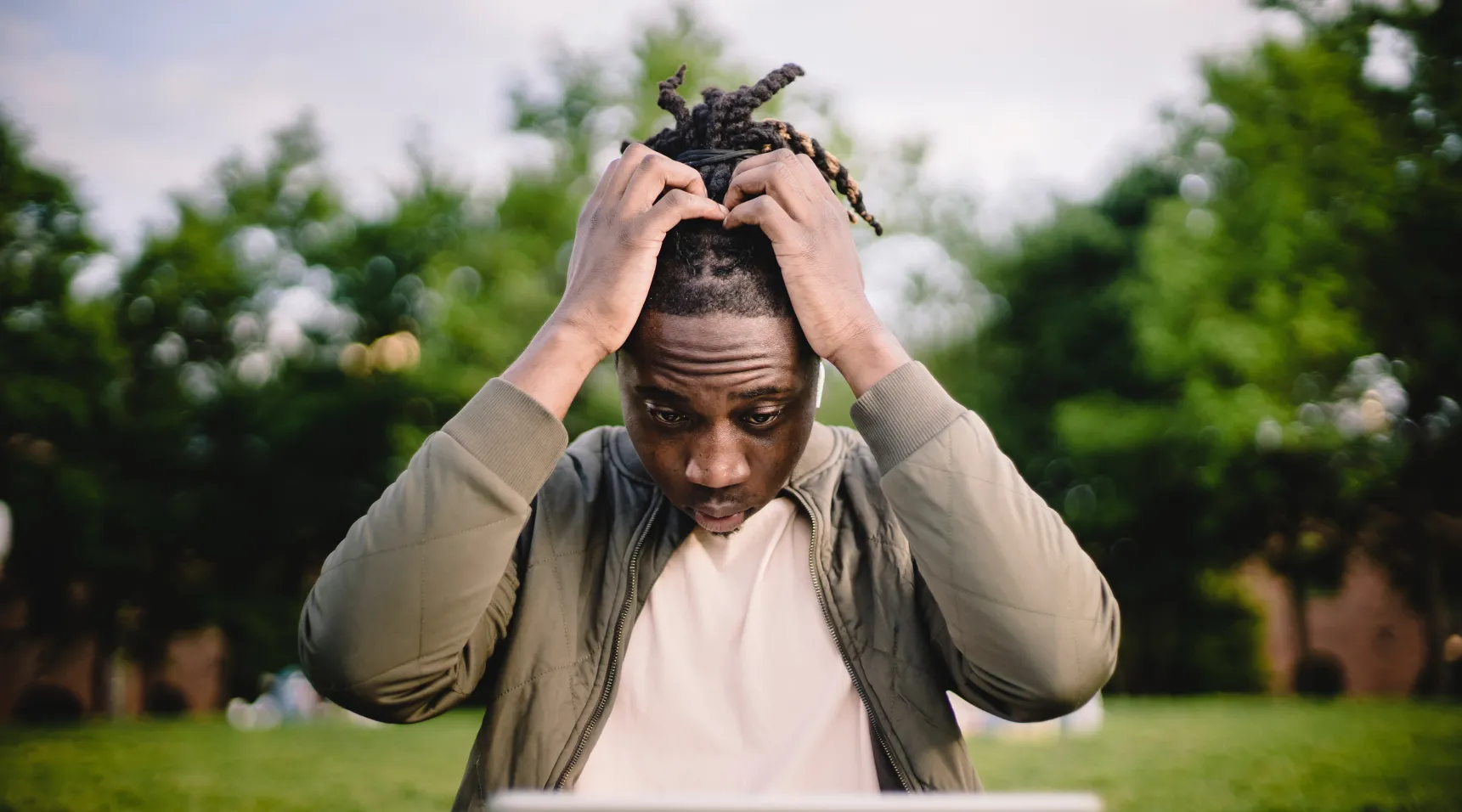 Man holding his head in frustration while looking at laptop outdoors, showing stress or overwhelm.