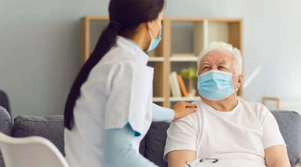 Support worker wearing a mask assisting an elderly client at home — ShiftCare SIL support.