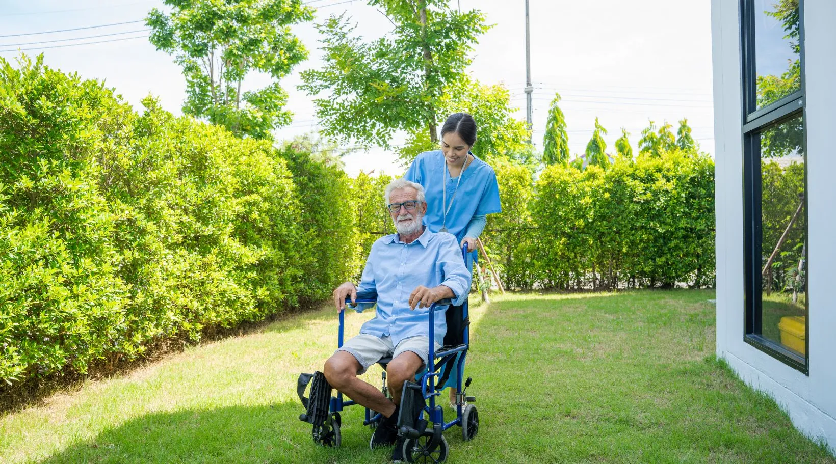 ShiftCare caregiver supporting elderly man in wheelchair outdoors.