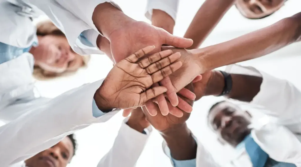 Care team stacking hands together representing collaboration and teamwork in home care services.
