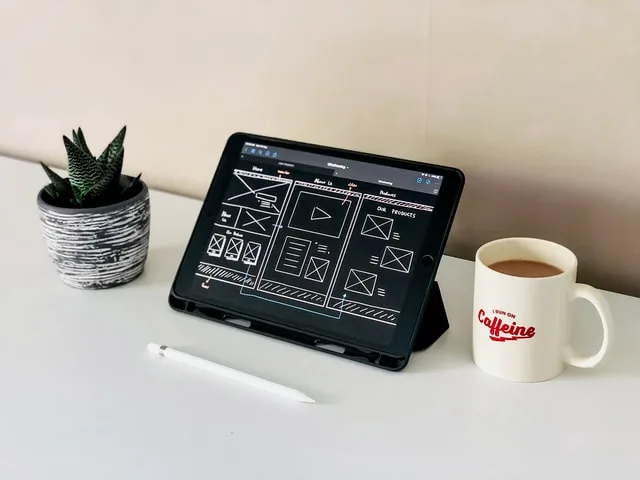 Tablet showing a UX design wireframe beside coffee and a plant, symbolizing creative digital workspace.