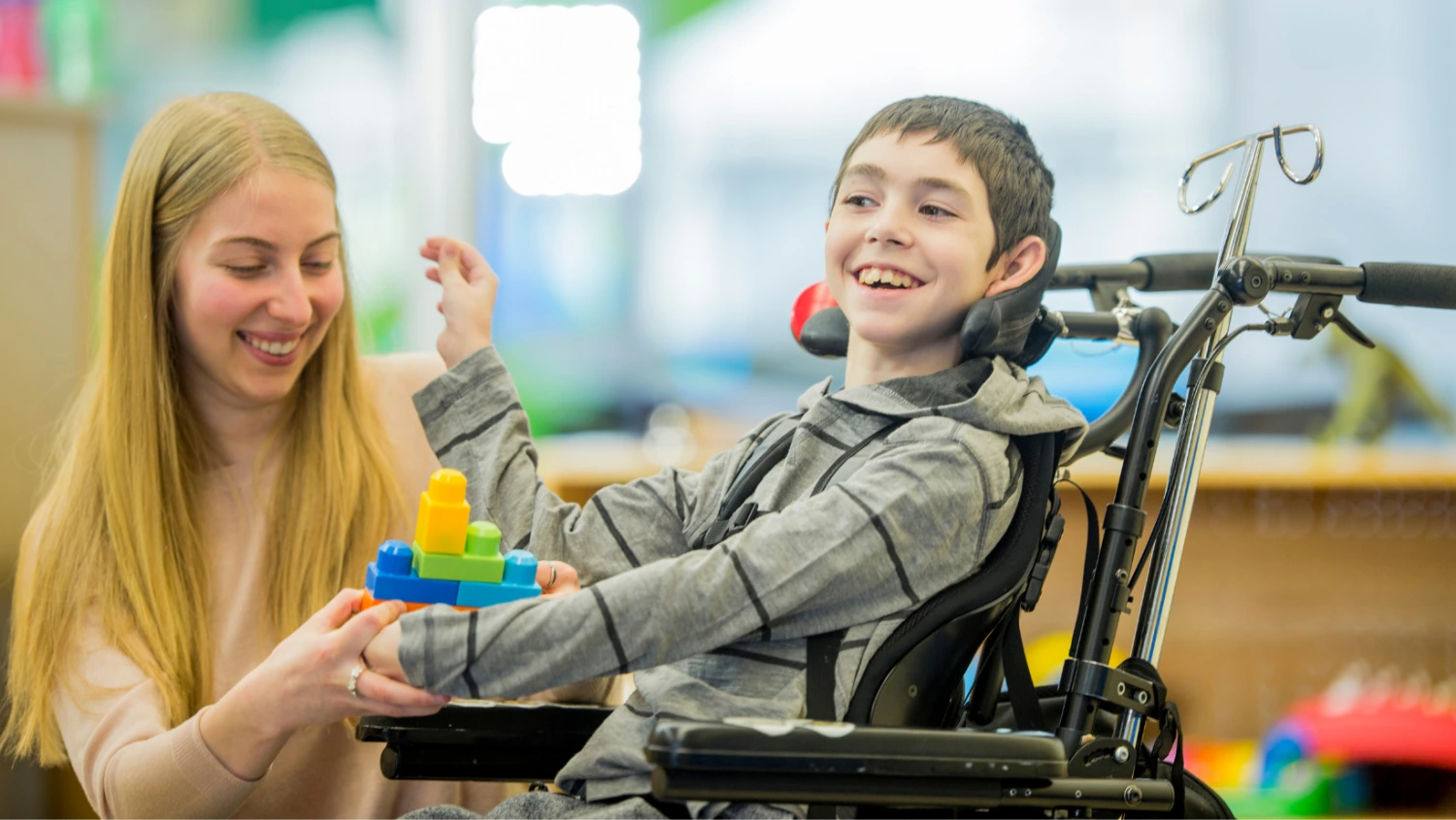 Smiling boy in wheelchair supported by ShiftCare worker during disability care activity.
