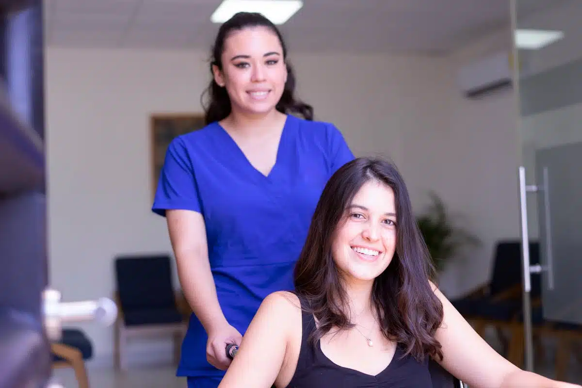A caregiver in blue scrubs attending to a woman in a wheelchair
