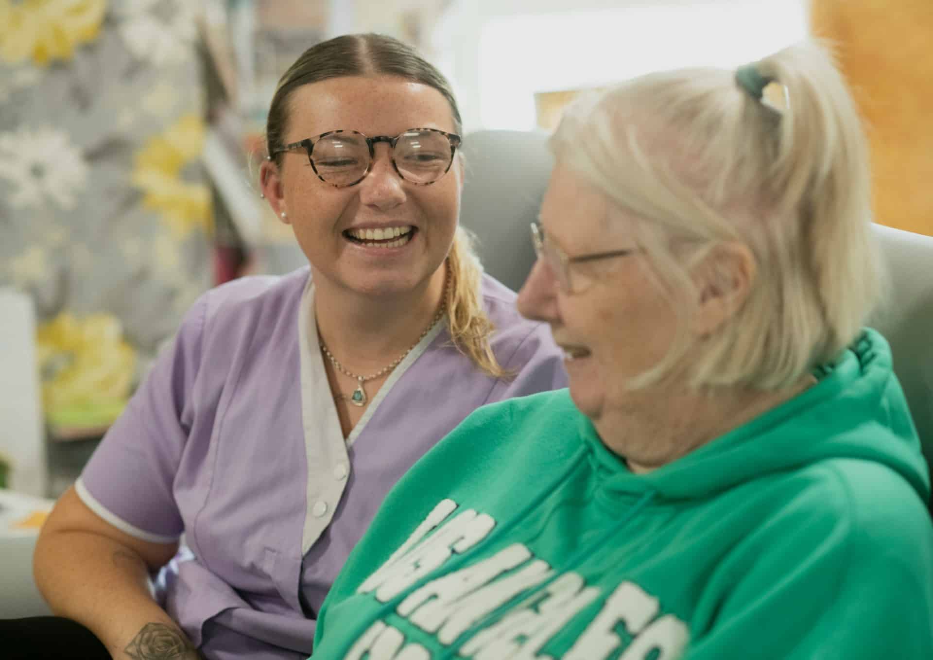 A carer in a purple shirt laughing with an older adult