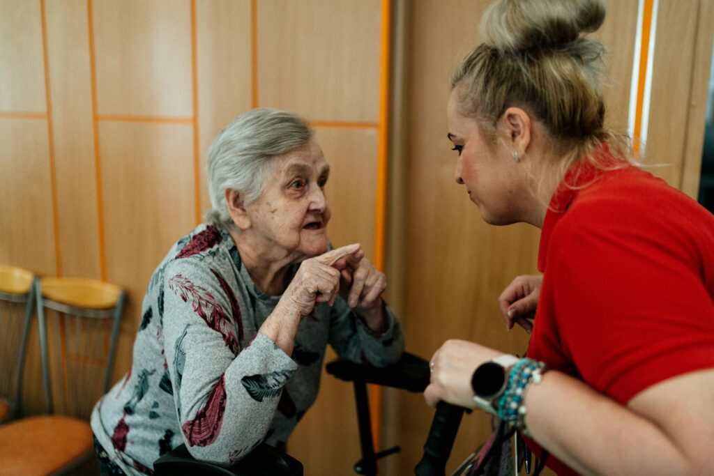 Carer in red shirt helping older adult participant stand up