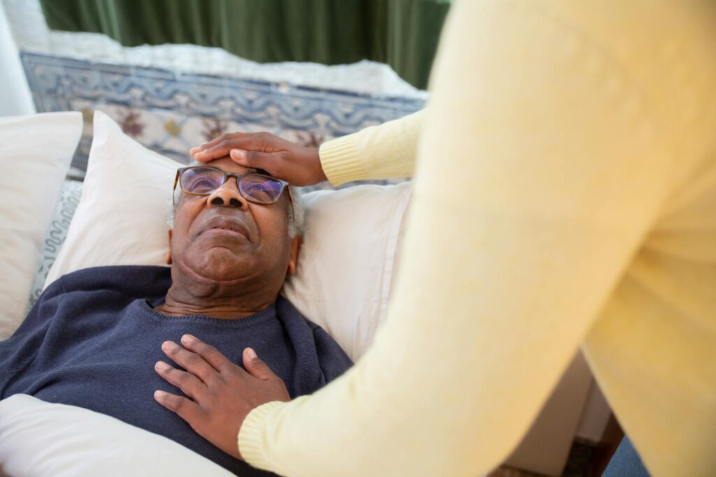 Elderly client lying down on a bed with carer in yellow shirt